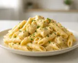 Penne z kawałkami kurczaka w kremowym sosie serowym, posypane natką pietruszki. Pyszne danie, które z pewnością zadowoli każdego miłośnika kurczaka w sosie serowym.