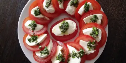 Pyszne pomidory z mozzarellą, ułożone na talerzu, ozdobione ziołami. Idealna przekąska na lato.