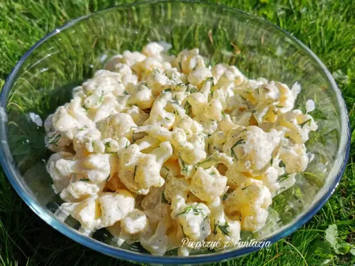 Kremowa, najlepsza sałatka z kalafiora z koperkiem, podana w szklanej misie na trawie.