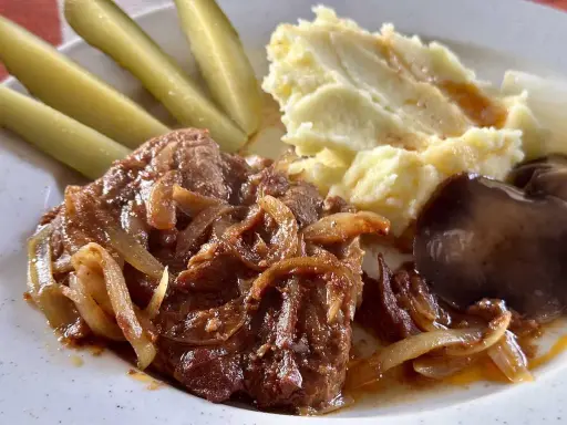 Karkówka pieczona w plastrach z cebulą, podana z puree ziemniaczanym, ogórkami kiszonymi i grzybami.