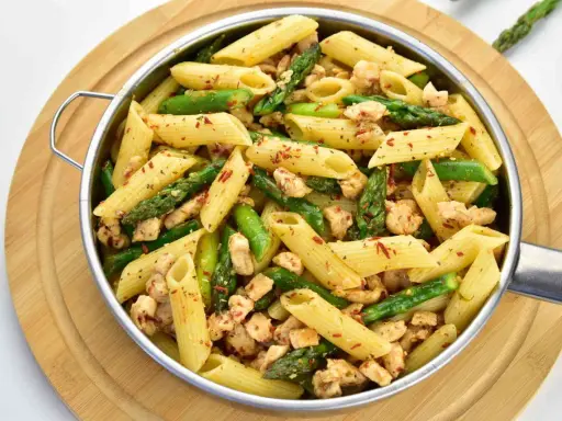 Penne z kurczakiem i szparagami, posypane płatkami chili. Pyszne danie na szybki obiad.