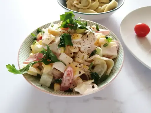 Pyszna sałatka z tortellini, jajka, kukurydzy i pomidorów, udekorowana natką pietruszki. Idealna na letnie dni.