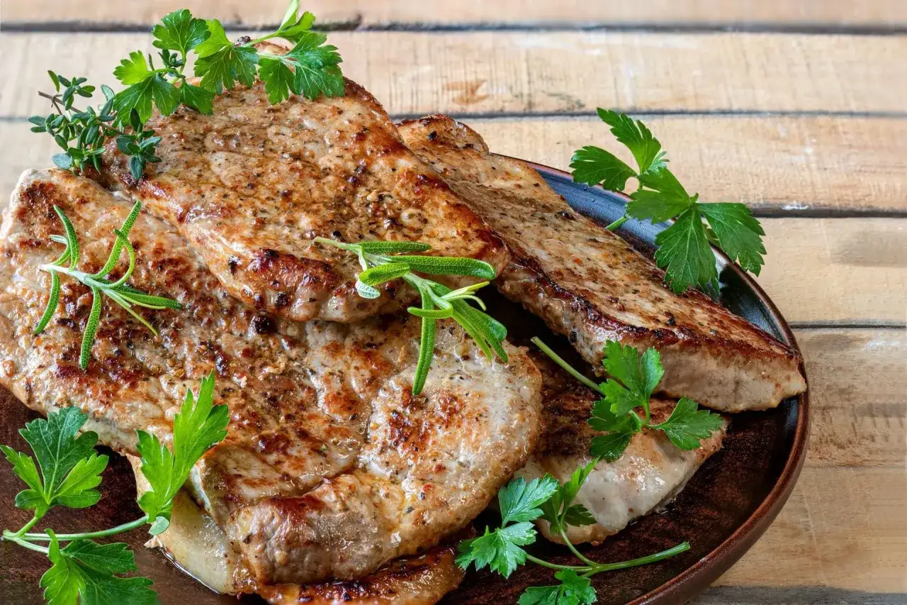 Soczysty schab z airfryer, przyprawiony ziołami, podany na talerzu z natką pietruszki i rozmarynem. Idealny obiad!