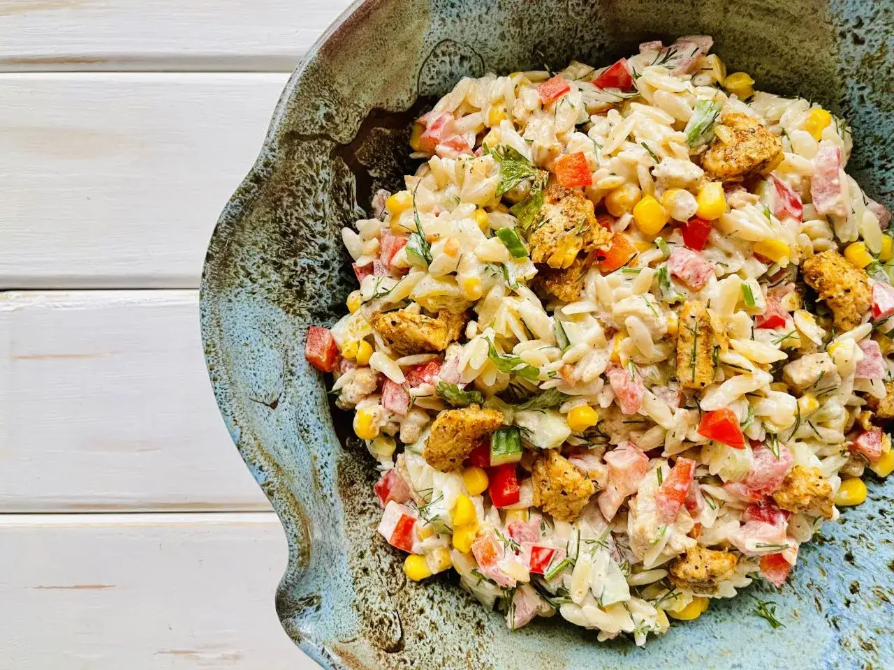 Pyszna sałatka z makaronem orzo, kurczakiem, kukurydzą i papryką, udekorowana świeżym koperkiem.