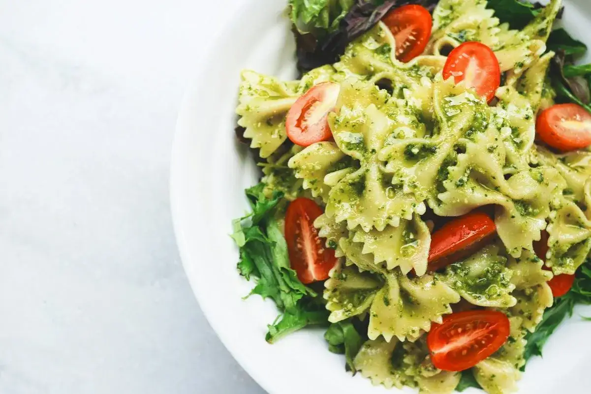 Pyszny makaron farfalle z aromatycznym pesto bazyliowym, udekorowany połówkami pomidorków koktajlowych i świeżą sałatą.