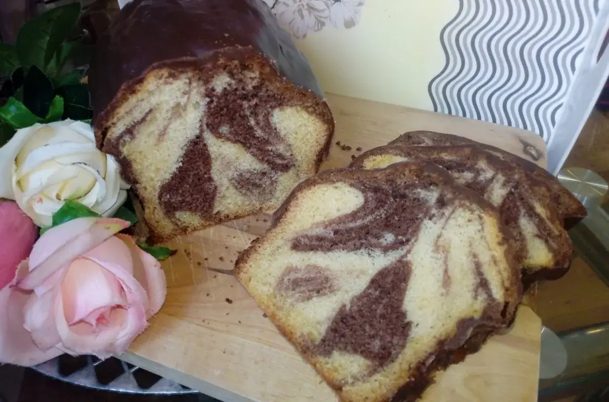 Pyszna babka na oleju z czekoladową polewą, pokrojona na plastry, obok piękne róże.