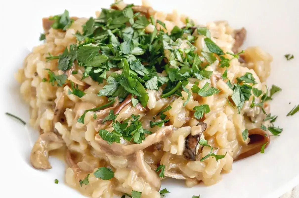 Kremowe risotto z grzybami, posypane świeżą natką pietruszki, prezentuje się apetycznie na białym talerzu.